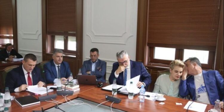 FOTOLAJM- Dumani në Kuvend, Flamur Noka i flet në vesh Kryemadhit, veshur mban bluzën “Lironi Berishën!”