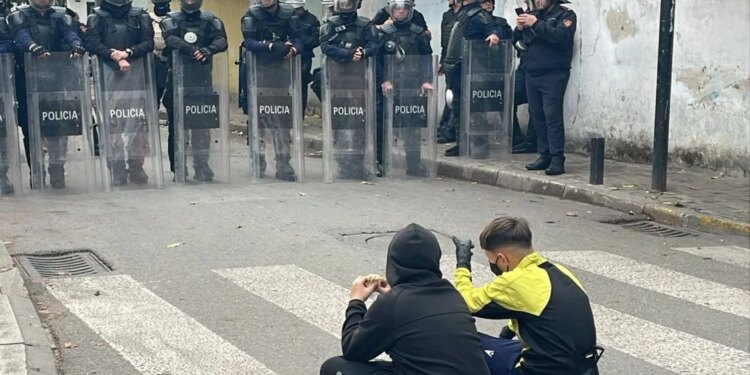 Protesta para Ministrisë së Arsimit: Dy protestues të vegjël maskuar ulen këmbëkryq para efektivëve, njëri valëvit flamurin shqiptar