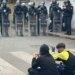 Protesta para Ministrisë së Arsimit: Dy protestues të vegjël maskuar ulen këmbëkryq para efektivëve, njëri valëvit flamurin shqiptar